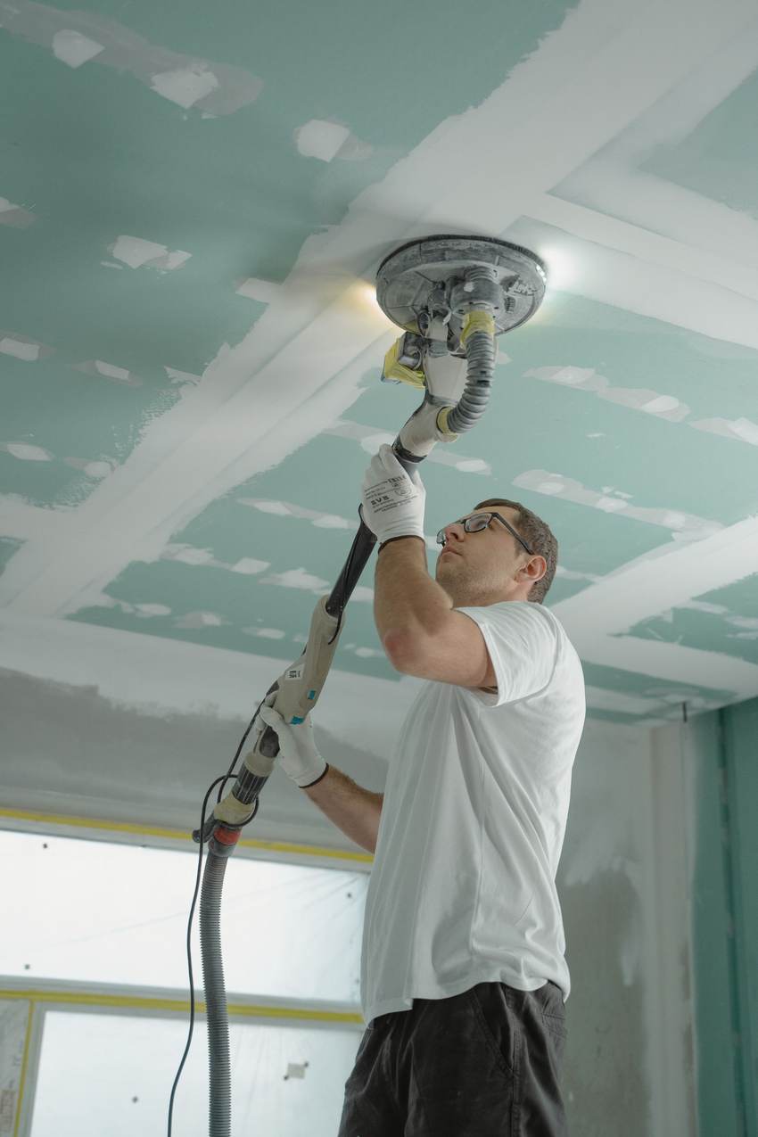 Worker sanding a smooth drywall ceiling